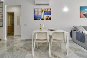Een moderne woonkamer met een eetgedeelte, een grijze bank en een schilderij van een kustlandschap.