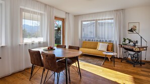 A modern living room with a wooden dining table, brown chairs, a yellow sofa, and a sewing machine. - Holiday Apartment 'Weitblick Kaltern' with Mountain View, Private Terrace, and Garden (Caldaro sulla strada del vino)