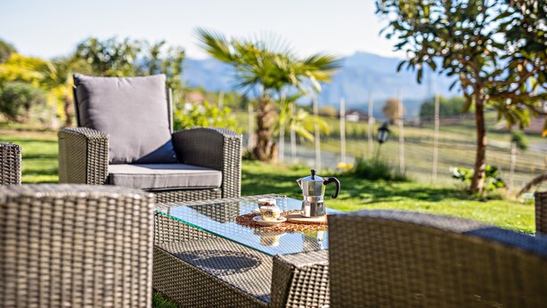An outdoor seating area with wicker furniture, a coffee table, and a view of the landscape. - Holiday Apartment 'Weitblick Kaltern' with Mountain View, Private Terrace, and Garden (Caldaro sulla strada del vino)