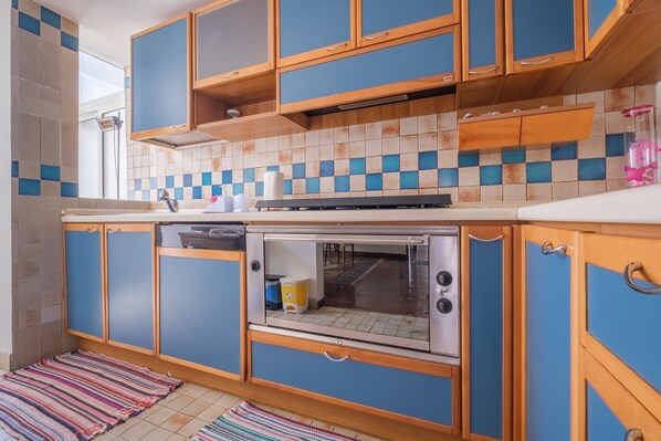Una cocina con armarios azules, un salpicadero de azulejos, un horno de acero inoxidable y un tapete a rayas.