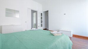 Une chambre avec une couvre-lit verte, une commode blanche, un banc blanc et une porte donnant sur un placard.