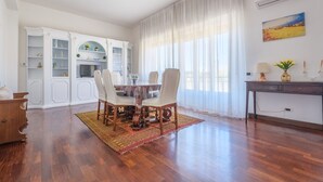 Un coin repas avec une table ronde, des chaises, un plancher en bois, un meuble blanc avec des étagères et une grande fenêtre avec des rideaux.