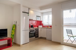 A compact kitchen with a microwave, oven, and dishwasher. A red cabinet and a window with curtains are visible.