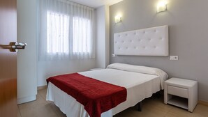 A bedroom with a bed, a bedside table, a nightstand, a window with curtains, and wall-mounted lights. - Apartment 'S22 Sa Caleta' with Sea View, Wi-Fi and Air Conditioning (Lloret de Mar)