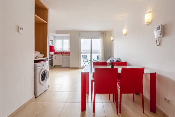 A modern kitchen with a washing machine, a dining area with red chairs, and a view to the outside.