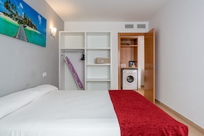 Ein Hotelzimmer mit Bett, roter Decke, einem Bild, einem Schrank, einer Waschmaschine und einer Dusche.