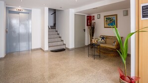 A hotel lobby with a staircase, a reception desk, a sofa, and a plant.