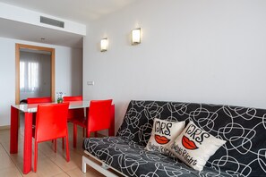 Un espace de vie moderne avec un canapé noir, des fauteuils rouges, une table à manger en verre et deux lampes fixées au mur.