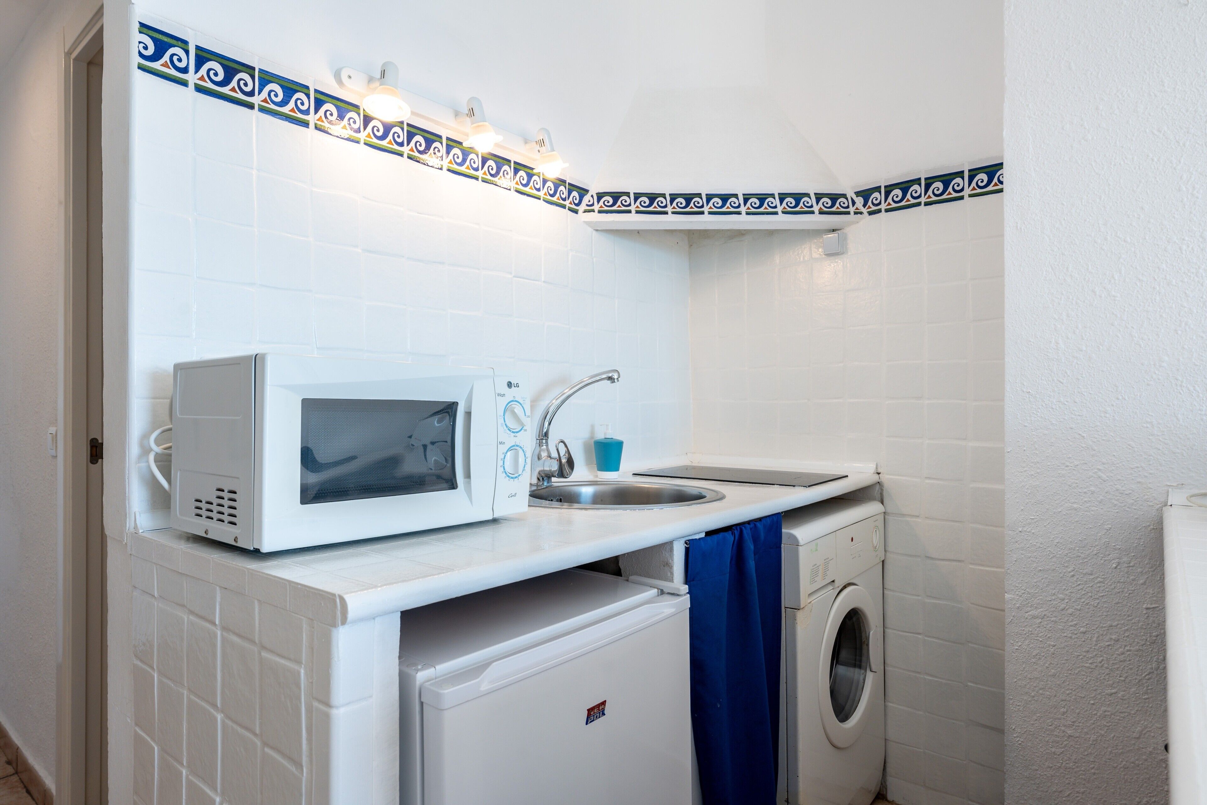 Une cuisine compacte équipée d’un four à micro-ondes, d’un évier et d’un lave-linge.