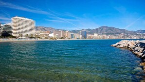 Un paysage urbain côtier avec une eau d’un bleu limpide, une côte rocheuse et, au loin, une série d’immeubles de grande hauteur.