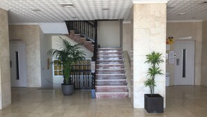 Un hall d’entrée spacieux avec un sol en marbre, un escalier doté d’une rampe en métal et des plantes en pot.