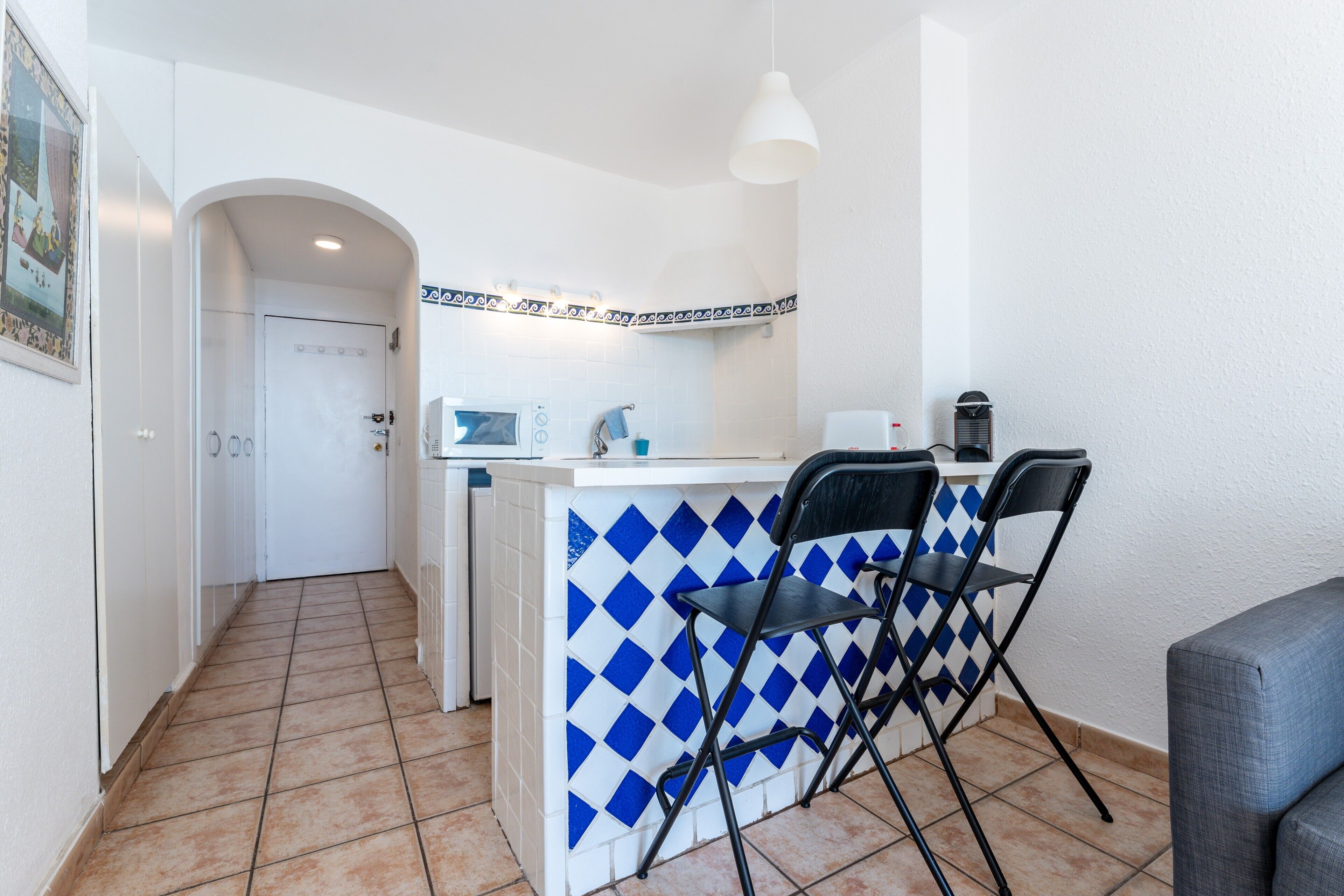 Cuina compacta amb salabost d'azulejos, microones, cafetera i dues cadires.