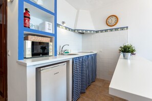 Una cocina compacta con microondas, pileta y heladera pequeña.