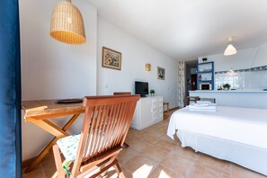 Una habitación con cama, escritorio, silla, televisor y kitchenette.