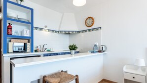 A kitchen with a white countertop, blue shelving, a wicker chair, a white cabinet, a clock, and a potted plant. - Studio apartment 'Ventana al Mar' with sea-facing terrace and air conditioning (Fuengirola)