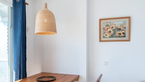 A room with a wooden table, a wicker pendant light, a framed floral painting, and a blue curtain. - Studio apartment 'Ventana al Mar' with sea-facing terrace and air conditioning (Fuengirola)