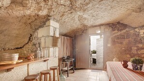 Una cucina rustica con un muro in pietra, sgabelli da bar in legno, pavimento piastrellato e vista attraverso una porta aperta.