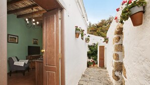 Un stretto sentiero in pietra conduce a un edificio rustico con una porta in legno, una televisione in una stanza e vasi di fiori pensili.