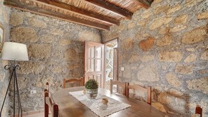 Una sala da pranzo rustica con parete in pietra, tavolo e sedie in legno, una pianta in vaso e una lampada.