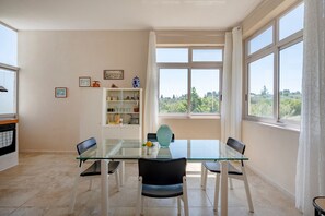 Un coin repas comprenant une table en verre, quatre chaises, un vase et une étagère ornée d’objets décoratifs.