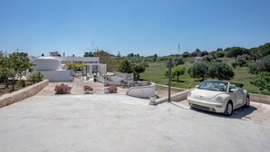 A parking area with a white convertible car, a modern building with a unique architectural design, and a landscaped garden with various plants and trees. - Villa 'Stellina e Trullo Cecé' with Private Terrace, Wi-Fi and Air Conditioning (ostuni)
