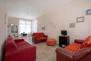 Un salon avec un canapé, un pouf et un téléviseur posé sur un meuble.