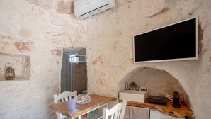 A kitchen with a stone wall, a wooden table, white chairs, a white refrigerator, a flat-screen TV, and a small sink. - Villa 'Stellina e Trullo Cecé' with Private Terrace, Wi-Fi and Air Conditioning (ostuni)
