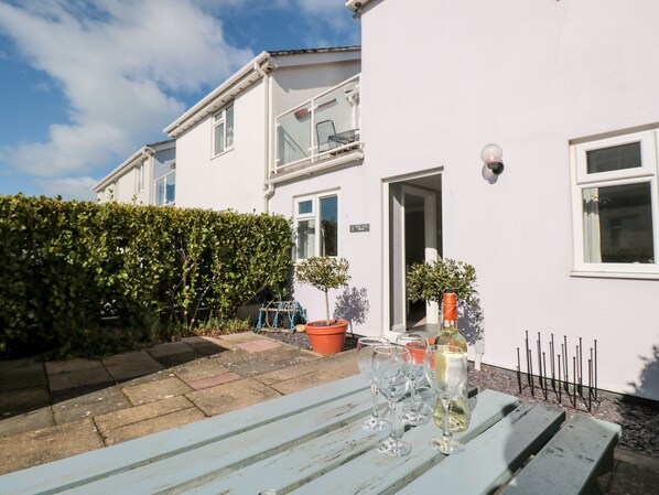 A white building with a door and windows, a hedge, and a table with wine glasses and a bottle. - 3 West Park Mews (Kingsbridge)