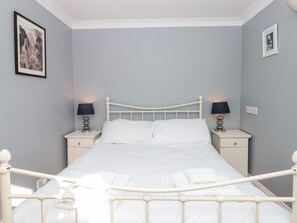 A neatly made bed with white bedding and a headboard, flanked by two bedside tables with lamps, in a room with light blue walls and framed pictures on the walls. - 3 West Park Mews (Kingsbridge)