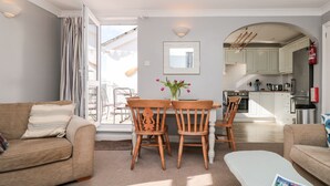 Una sala de estar moderna con un sofá, una mesa de comedor con sillas y una cocina visible a través de una puerta abierta.