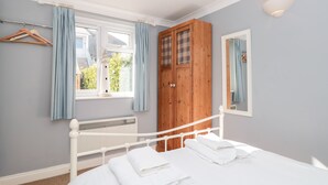 Un dormitorio con cama blanca, armario de madera, ventana con cortinas y un radiador.
