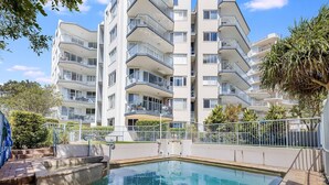 Een meerlaags appartementencomplex met balkons, een zwembad en een toegangshek.