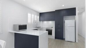 Een moderne keuken met een wit kookeiland, donkere kasten, een magnetron, een fornuis en een koelkast.