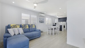 Een moderne woonkamer met een blauwe bank, een witte eettafel en plafondventilatoren.