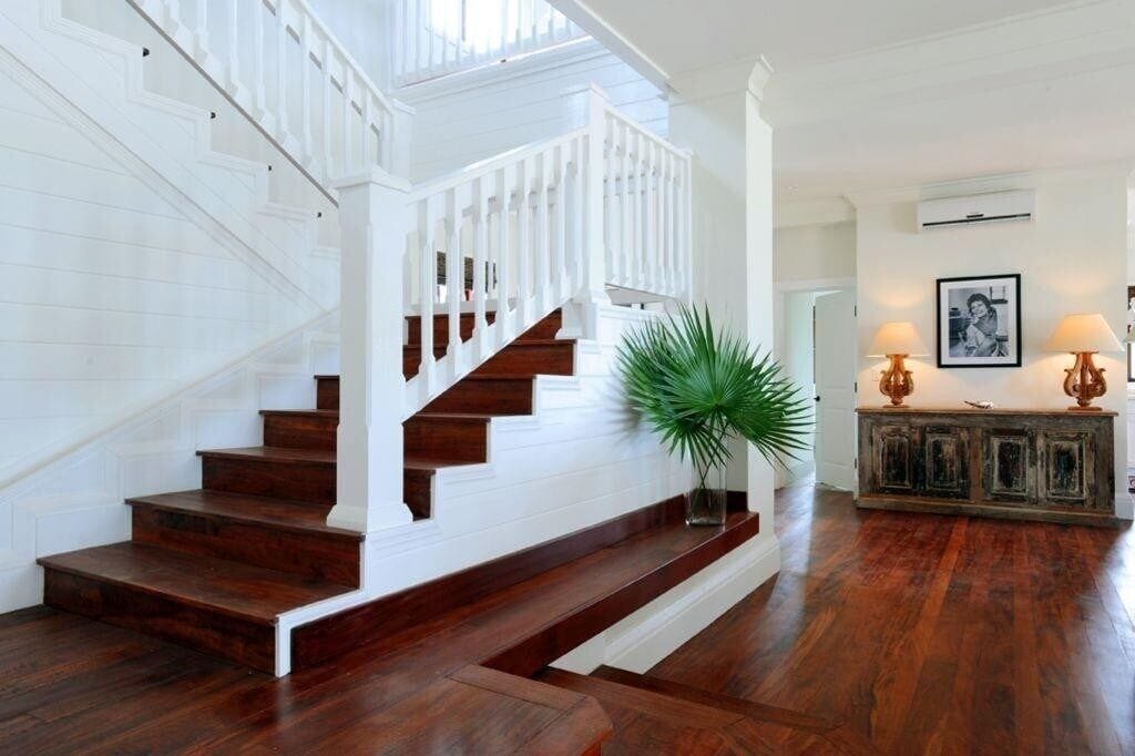 Un magnifique escalier avec des rampes blanches et des marches en bois foncé, menant à un palier agrémenté d’une plante en pot et d’une console sur laquelle sont posées des lampes.