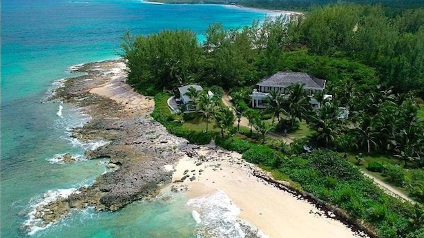 A coastal property with a beach, a house, and surrounding greenery.