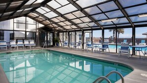 An indoor swimming pool with clear glass walls, blue lounge chairs, and a covered seating area. - 0910 Gone To The Beach by Atlantic Towers (Carolina Beach)