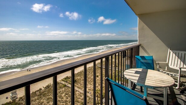 A balcony with a view of the ocean, a wooden table, and two chairs. - 0910 Gone To The Beach by Atlantic Towers (Carolina Beach)