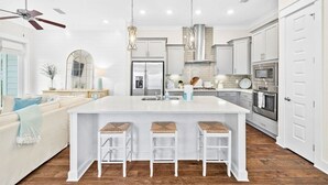 A modern kitchen with white cabinetry, a central island with stools, stainless steel appliances, and pendant lighting. - ✨ Modern 30A Stay | Golf Cart | Pool Access (Inlet Beach)