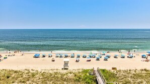 A beach with rows of blue umbrellas and a lifeguard tower. - 0609 Oceanfront Escape by Atlantic Towers (Carolina Beach)