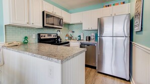 A kitchen with white cabinets, a stainless steel refrigerator, a microwave, a stove, and a dishwasher. - 0609 Oceanfront Escape by Atlantic Towers (Carolina Beach)