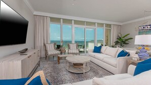 A spacious living room with a large TV, comfortable seating, a coffee table, and a view of the ocean. - Phoenix Gulf Towers 402 2 Bedroom Condo (Orange Beach)