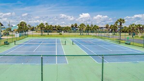 En tennisbana med två banor, omgiven av ett staket, och palmer i bakgrunden.