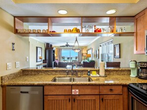 A kitchen with granite countertops, a stainless steel sink, wooden cabinets, and a view to a dining area.