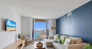 Una sala de estar moderna con un ventanal grande, un televisor de pantalla plana, un sofá, un sillón y una mesa de centro.