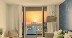 Quarto com vista para o pôr do sol sobre o horizonte da cidade, uma janela grande, um sofá, um abajur e um mapa na parede.