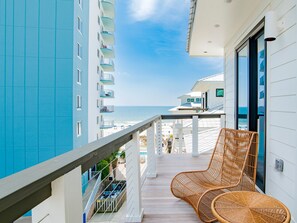 A balcony with wicker chairs overlooking a beach and a high-rise building.