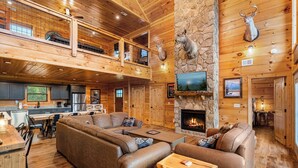 Amplia sala de estar con chimenea de piedra, un sofá modular grande y techo de madera.