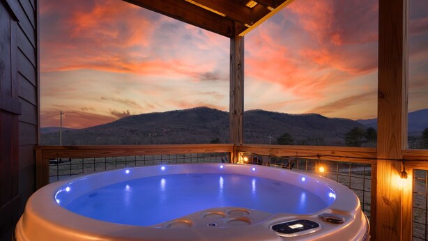 Un jacuzzi con terraza de madera y vista a las montañas durante el atardecer.