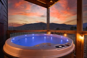 Un jacuzzi con terraza de madera y vista a las montañas durante el atardecer.